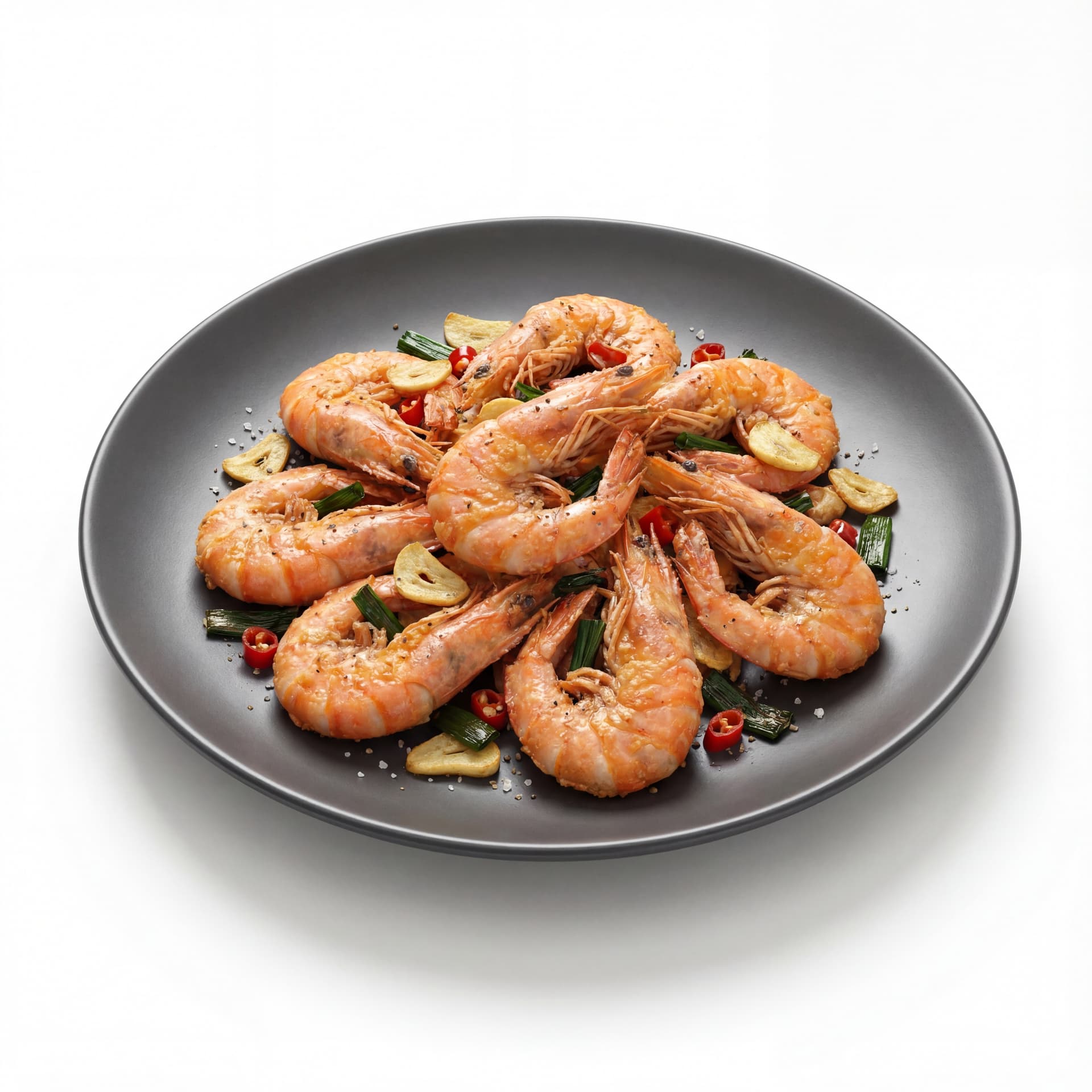 A dark round plate featuring salt-and-pepper shrimp with shell-on shrimp, sliced garlic, chopped chili, and fried scallions.